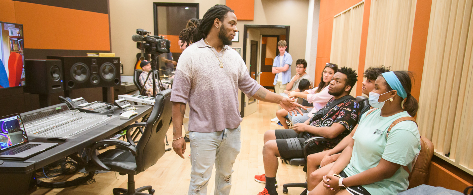 Man teaching a group of students in front of recording and mixing equipment