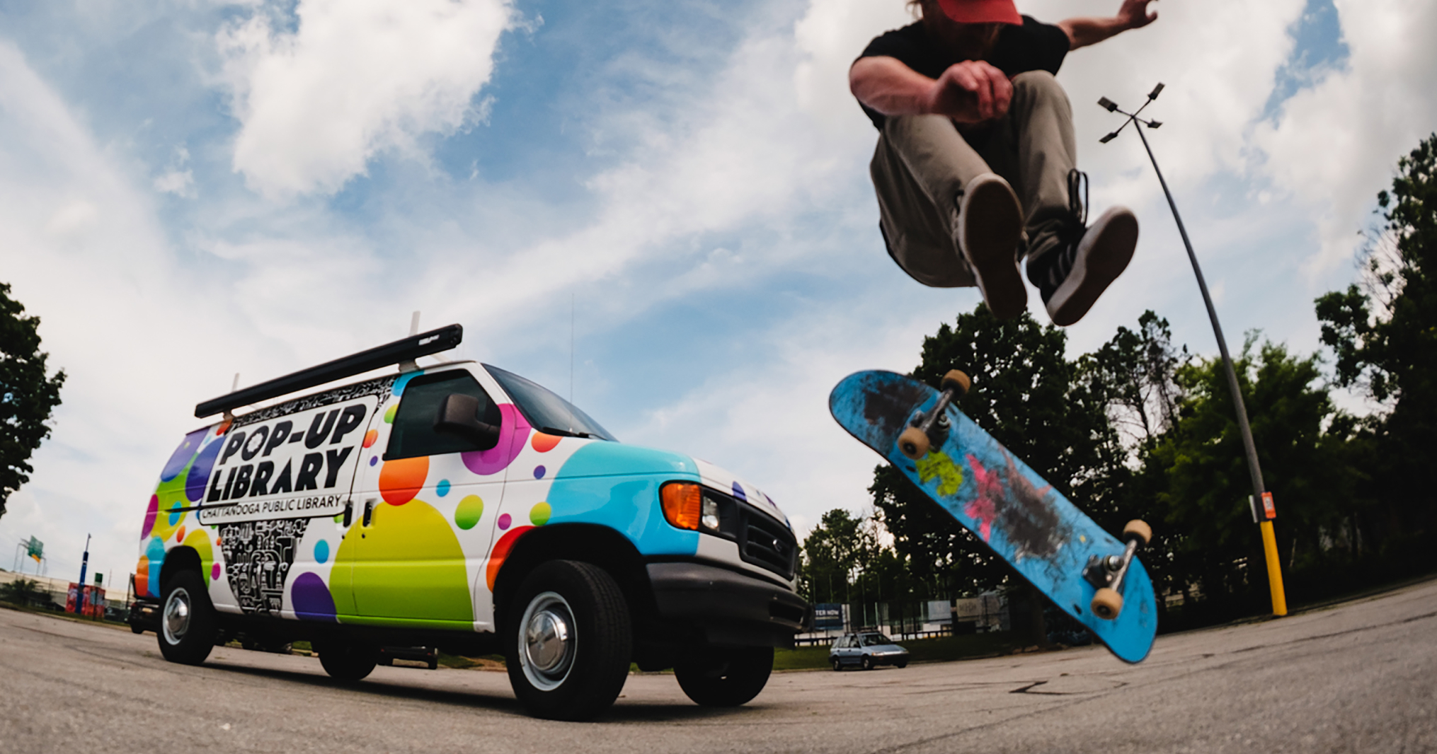 Man on skateboard doing a kickflip in front of the Pop-Up Library van